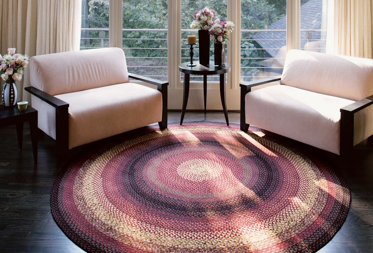 A large round braided rug in a bright sitting room between two armchairs