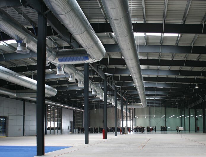 A large empty industrial hall with exposed steel columns and circular ventilation ducts along the ceiling