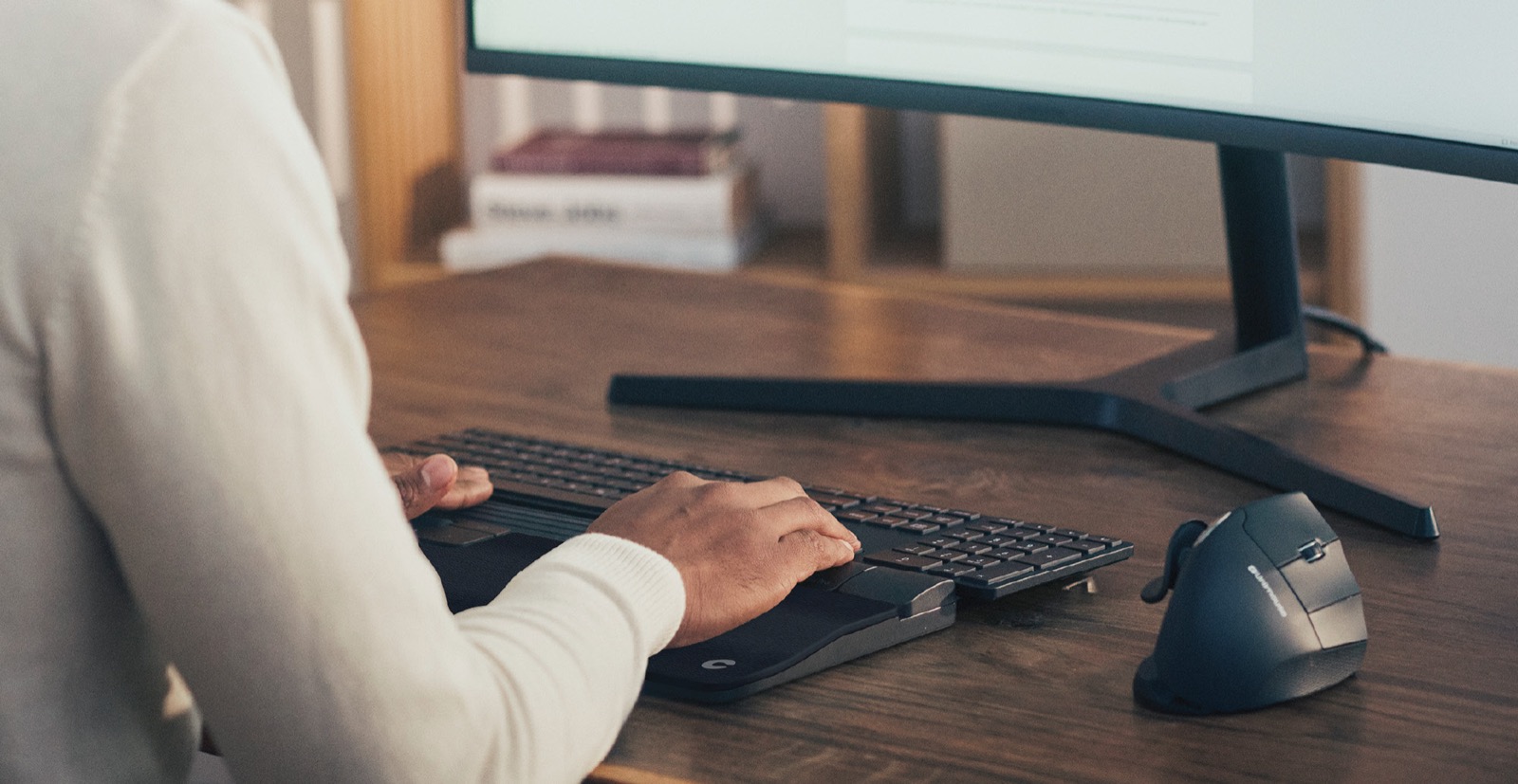 A RollerMouse and keyboard in use at a wooden desk beside a monitor