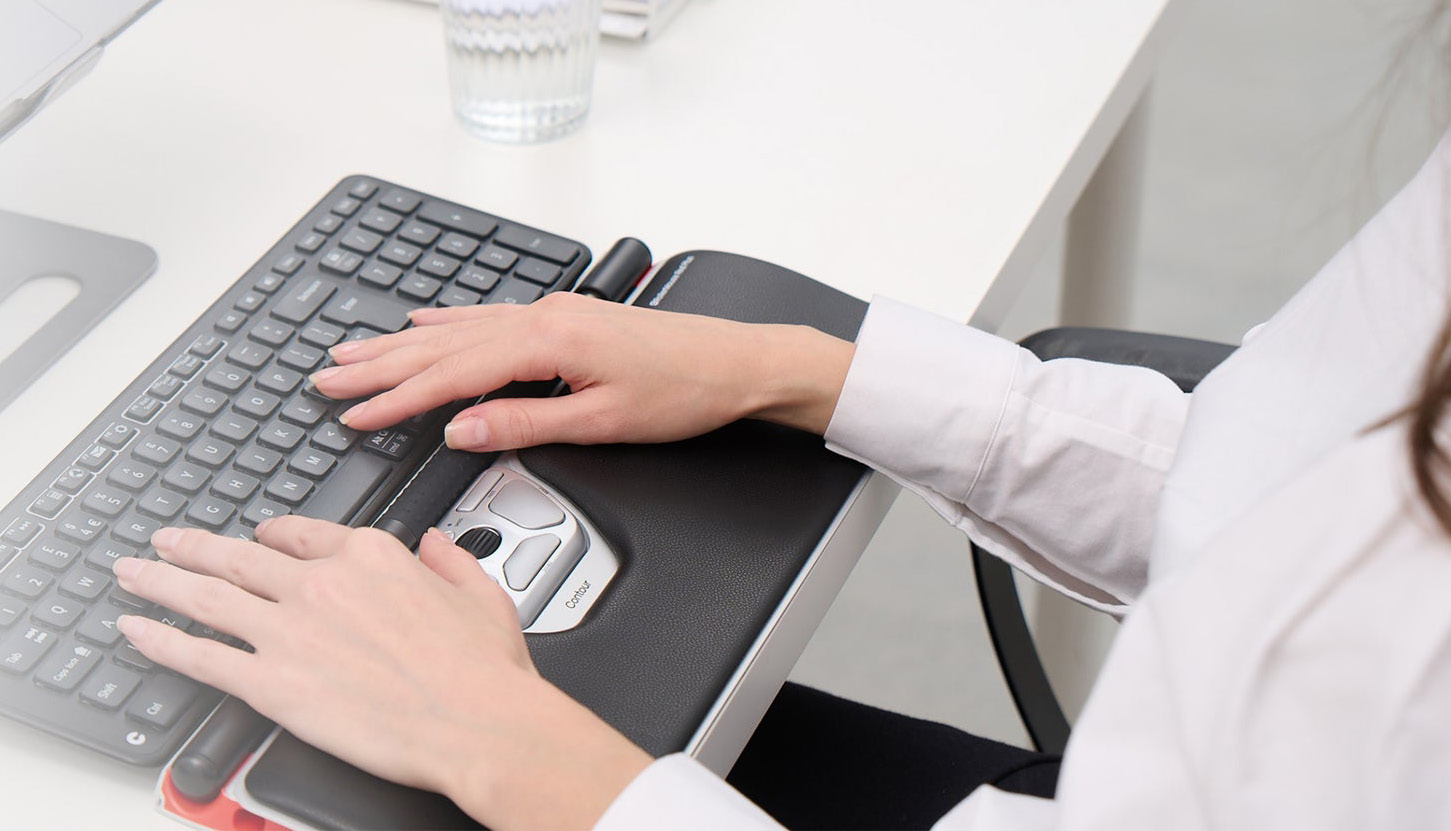 Hands using a Contour RollerMouse and keyboard at a white desk