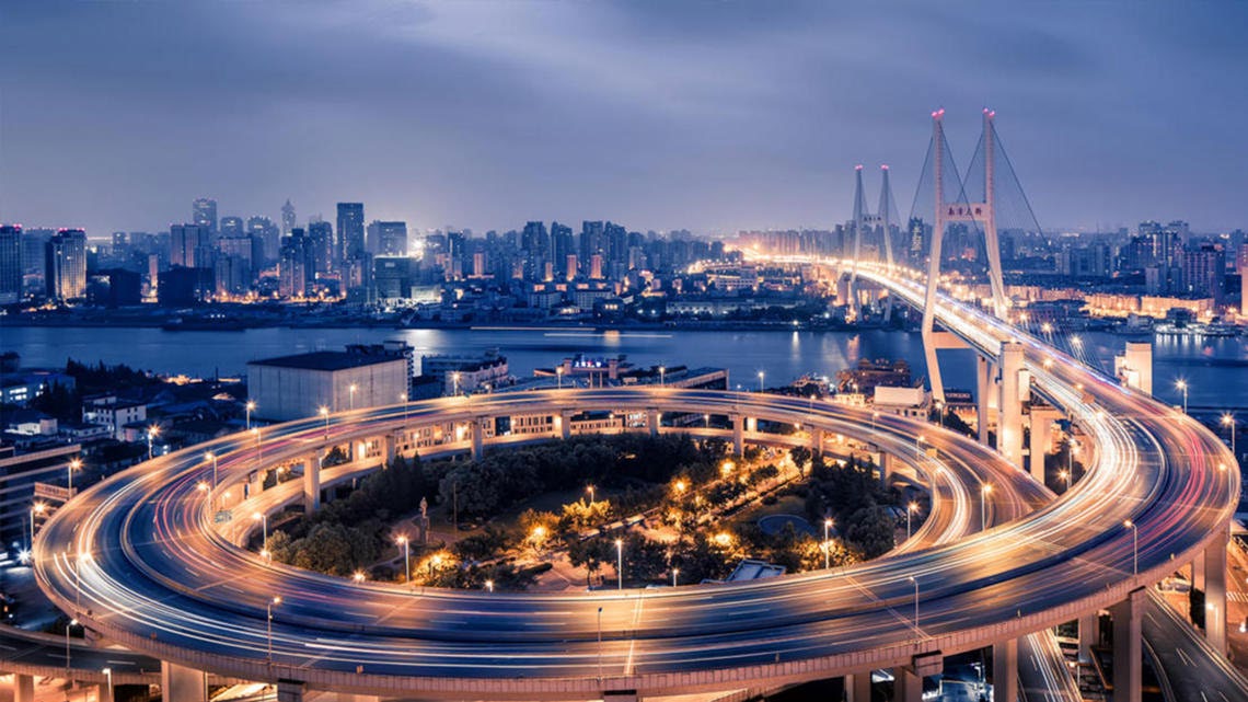 A multi-level road interchange at dusk, traffic drawn out into light trails