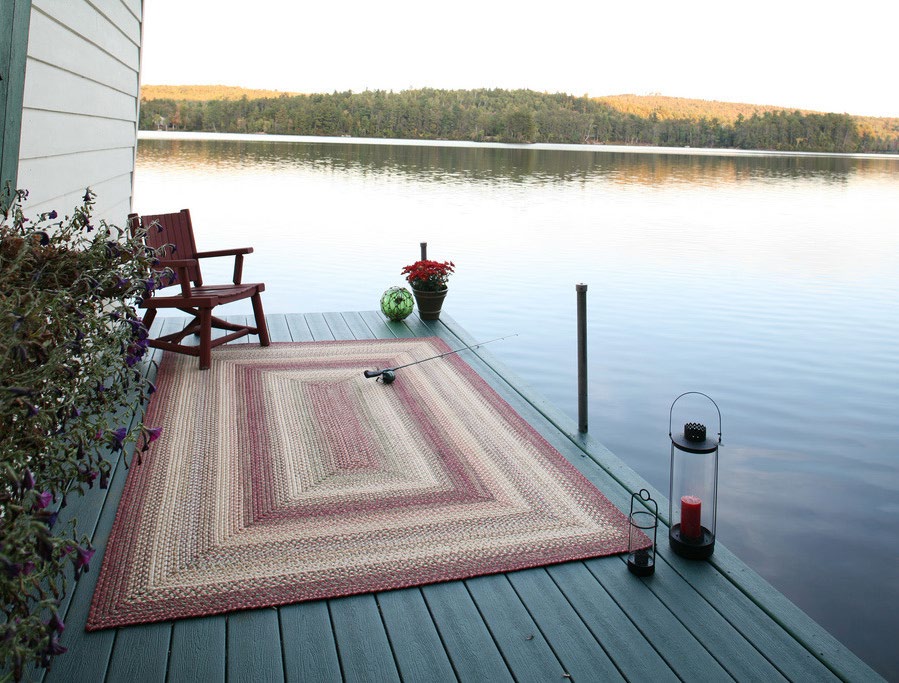 A braided rug laid on a wooden lakeside deck at dusk, with a chair and lanterns
