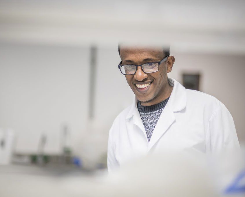 A smiling Expedeon scientist in a white coat and safety glasses in the laboratory