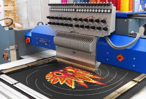 An embroidery head stitching a coloured design onto dark fabric held in a frame