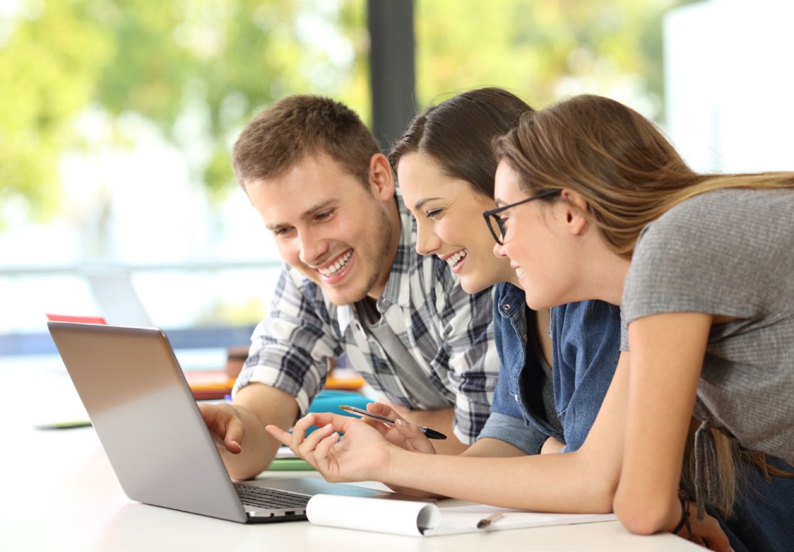 Three students looking at a laptop screen together and smiling