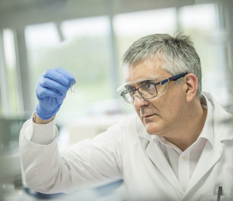 An Expedeon scientist in safety glasses holding a sample vial up to the light
