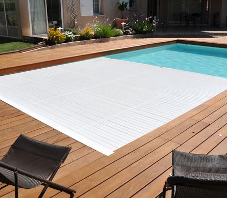A white slatted cover closed across a pool beside a terrace with chairs