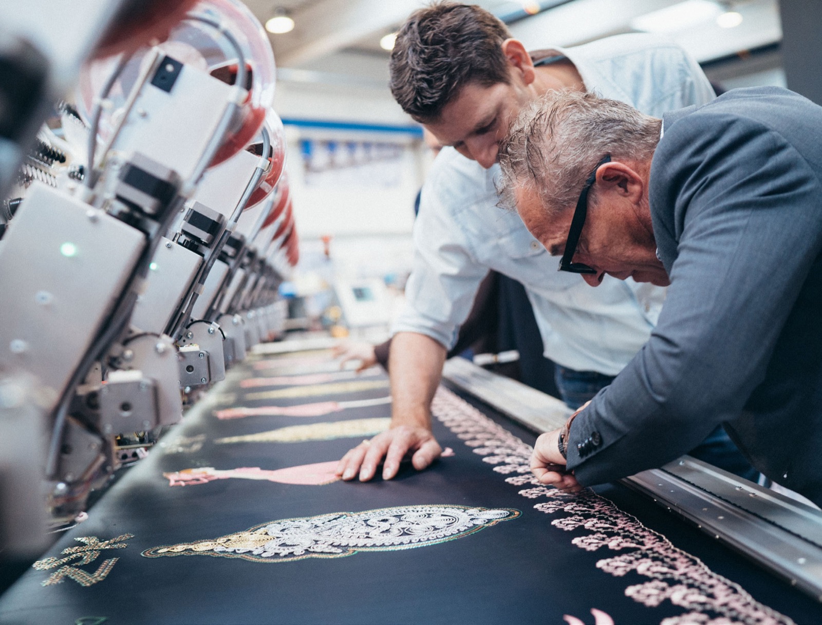 Two colleagues leaning over an embroidery machine to inspect a finished panel