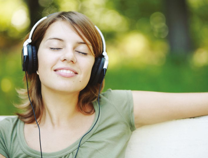 A woman outdoors wearing headphones with her eyes closed