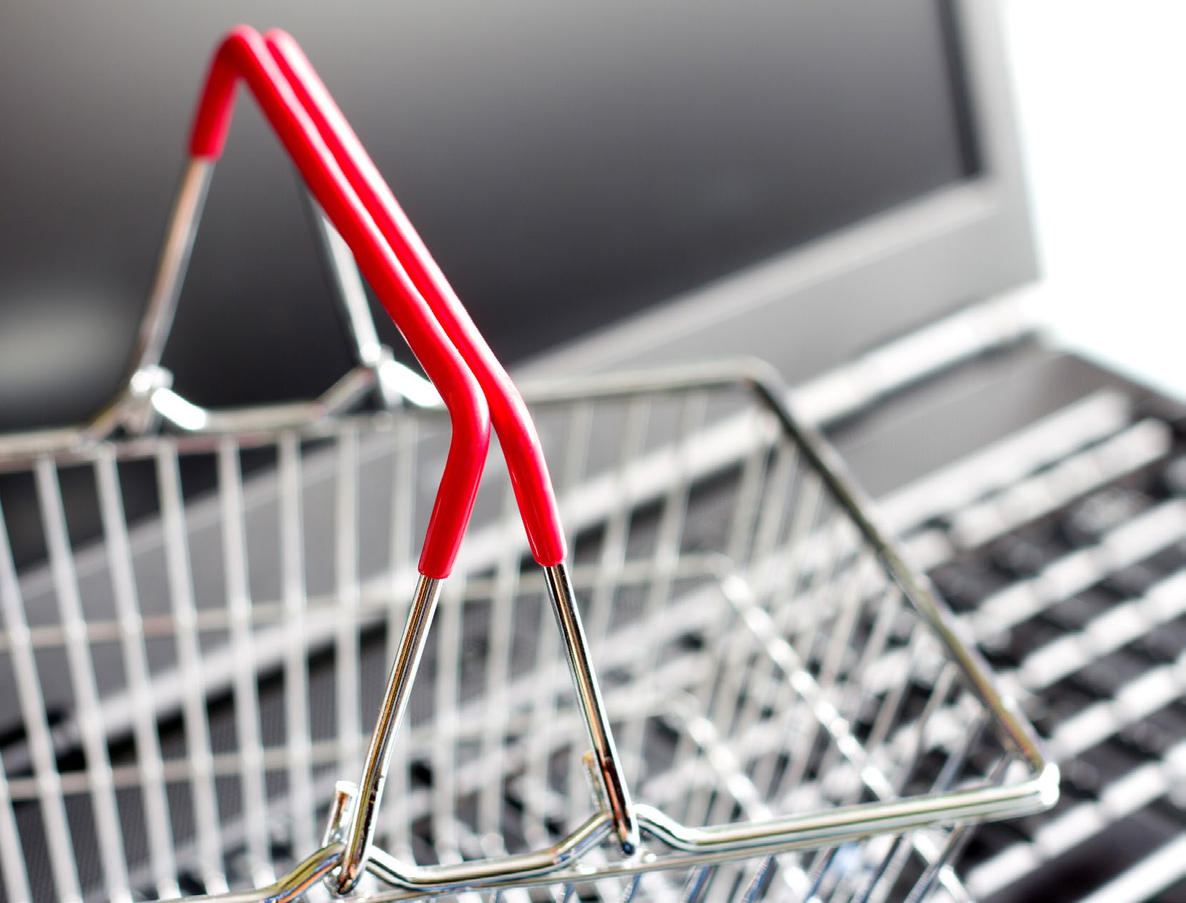 A small wire shopping basket standing on a laptop keyboard