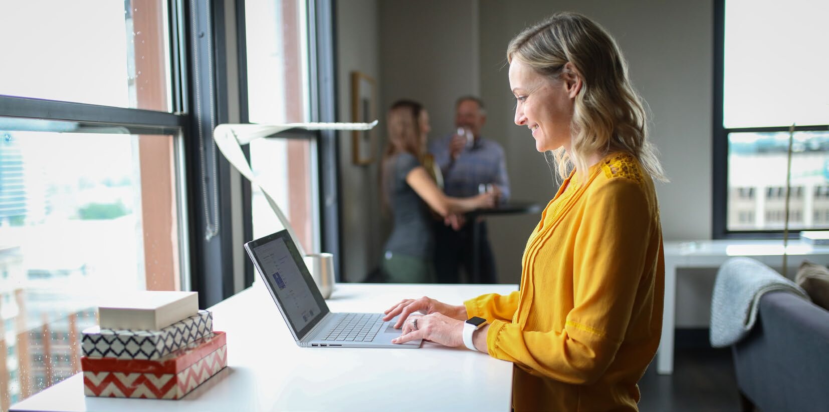 A woman working at a laptop on a standing desk in an open office