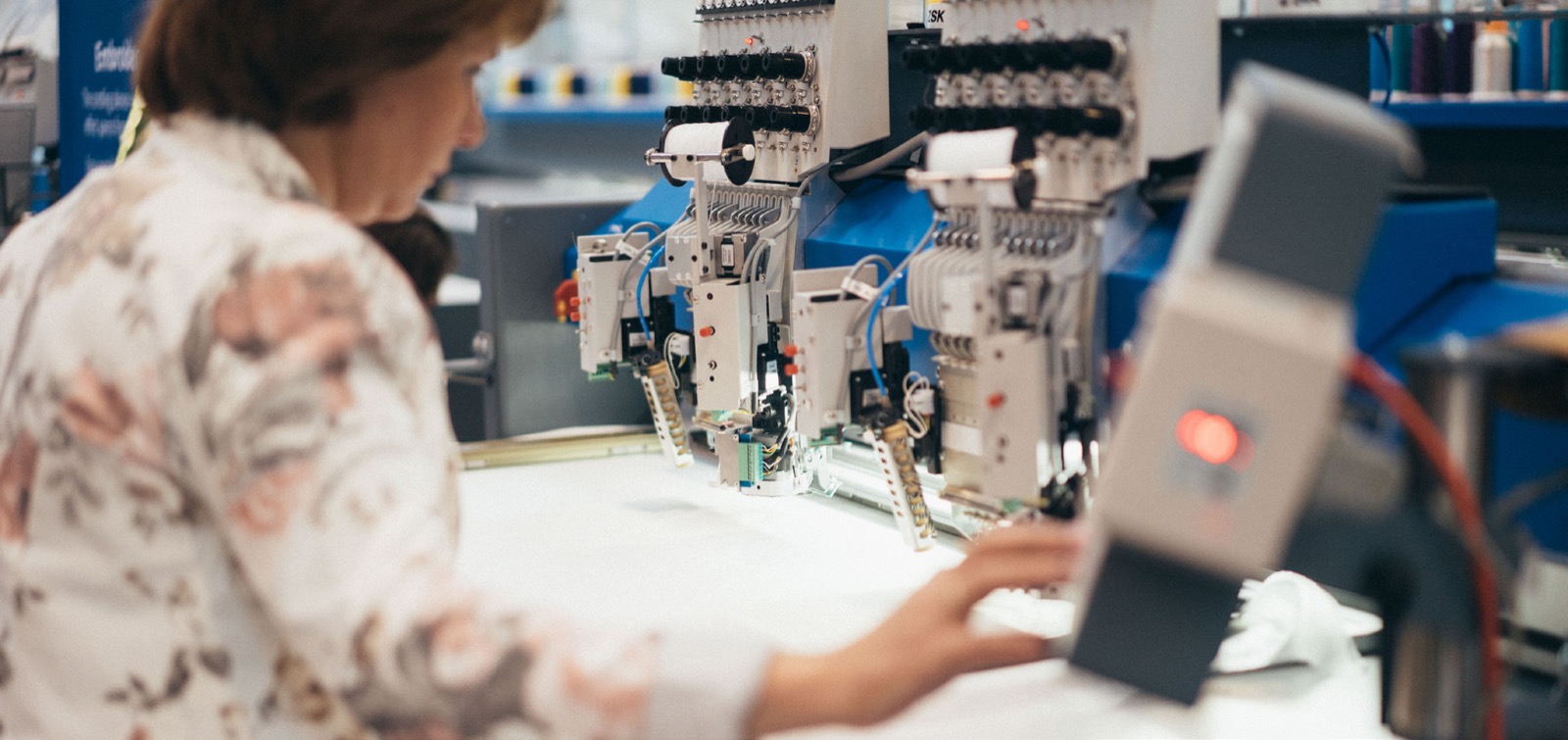 An operator working at a row of embroidery machine heads on the production floor