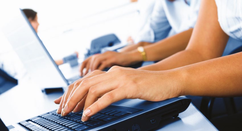 A row of people working side by side on laptops