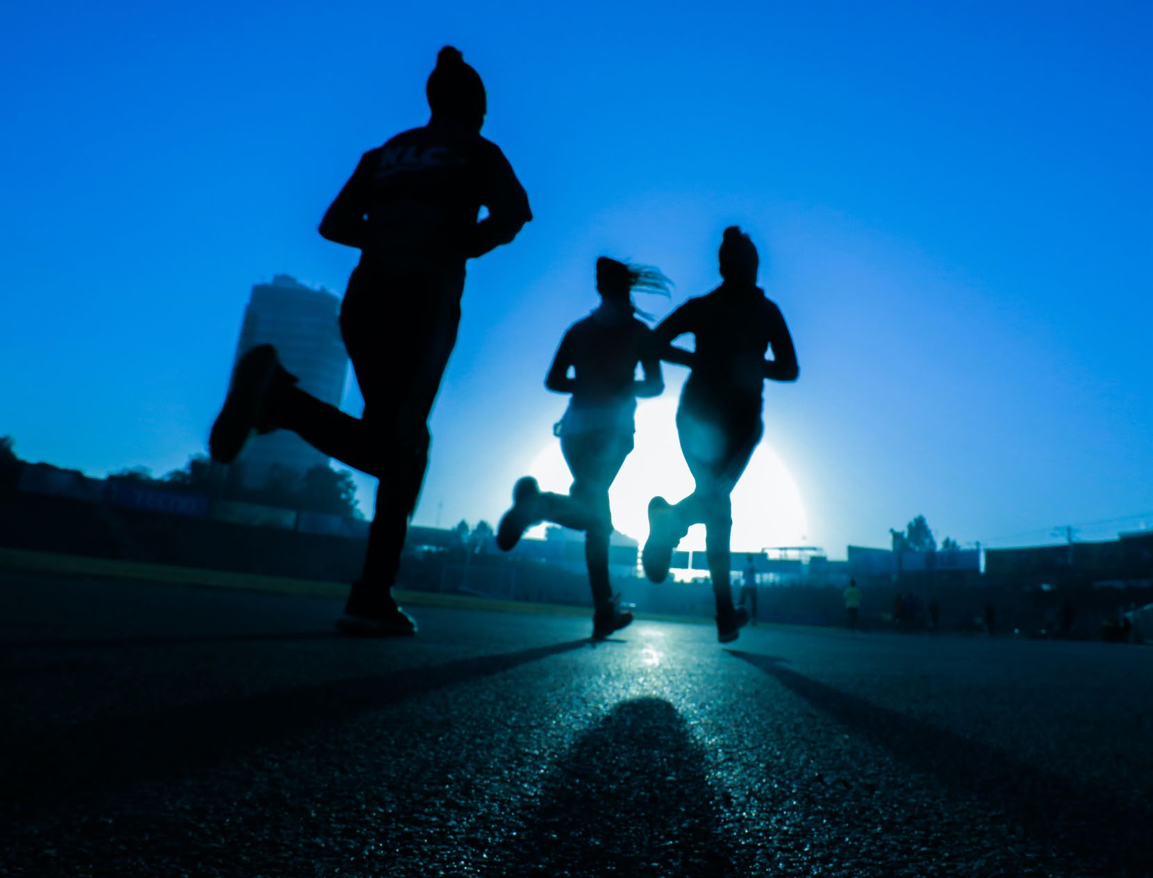Three runners silhouetted against the sunrise on a track